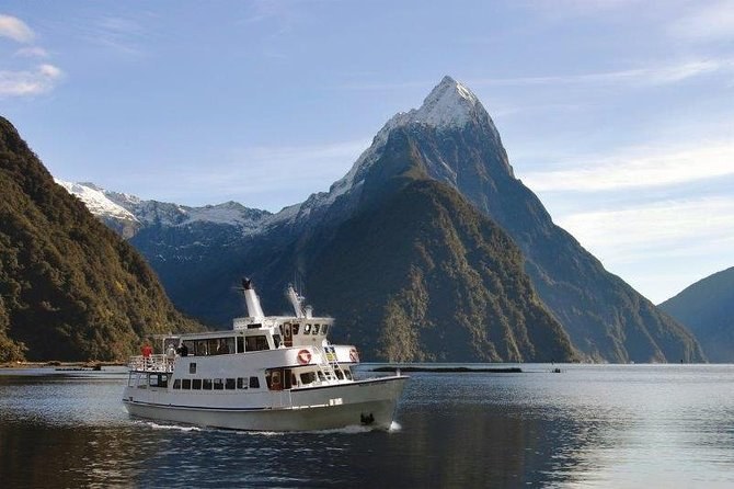 A white cruise boat on still water below a snow-streaked pointed peak