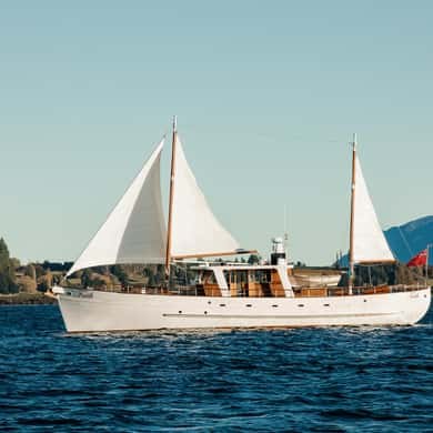 A white historic motor yacht under full sail on a lake