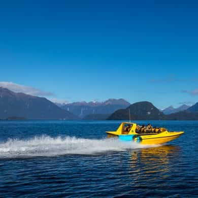 A yellow jet boat racing across a lake with mountains behind