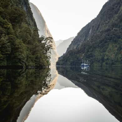 Forested walls reflected in a mirror-still fiord, a small boat far off
