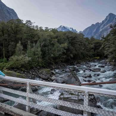 A clear mountain river running over stones below a footbridge rail