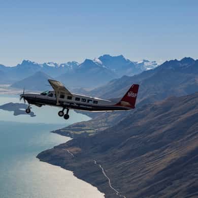 A small high-wing plane flying over mountains and a lake